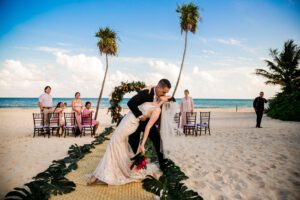 Groom dipping the bride for a romantic kiss on a sandy tropical beach after the ceremony, ideal scene for a luxury Cancun destination wedding.