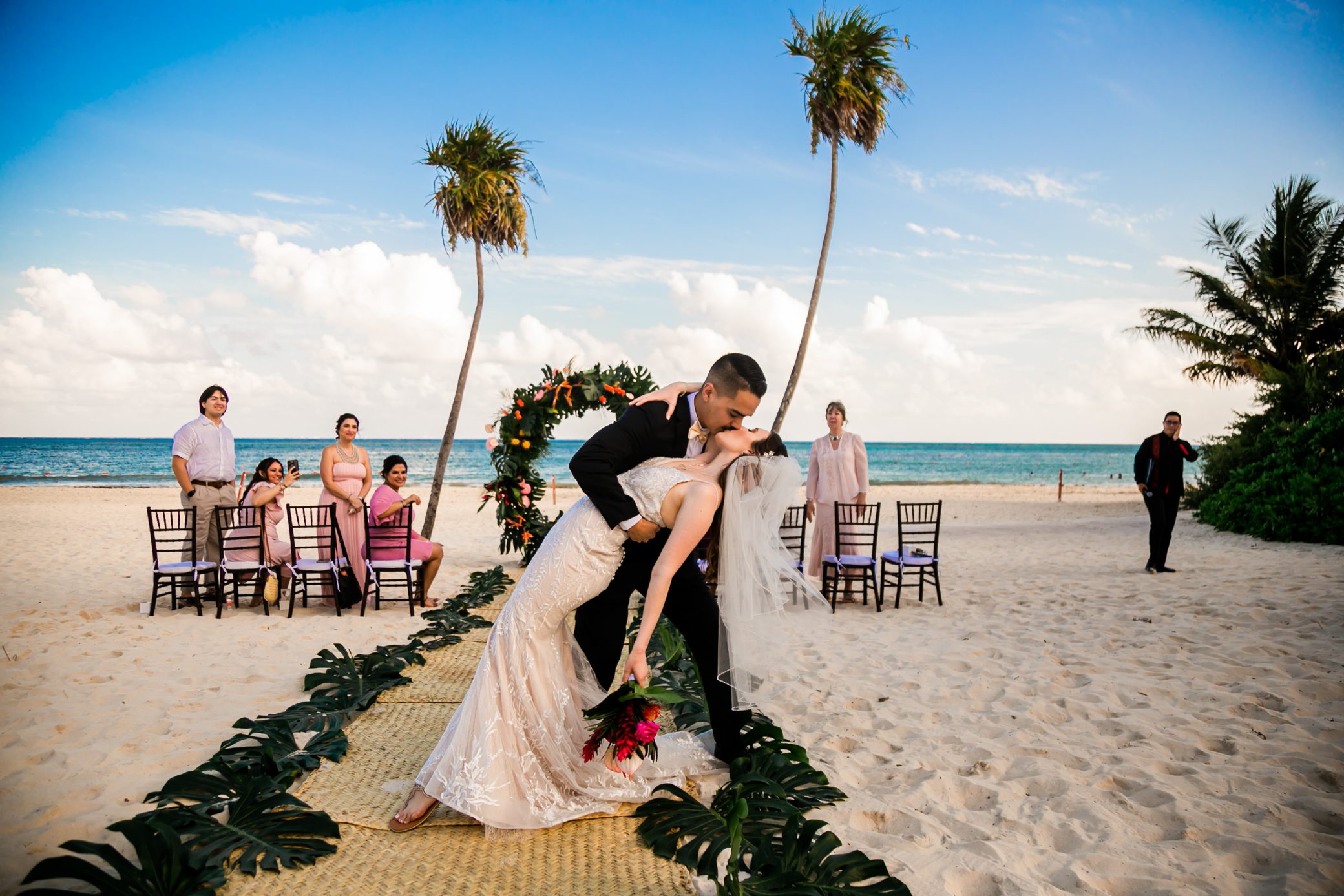 Groom dipping the bride for a romantic kiss on a sandy tropical beach after the ceremony, ideal scene for a luxury Cancun destination wedding.