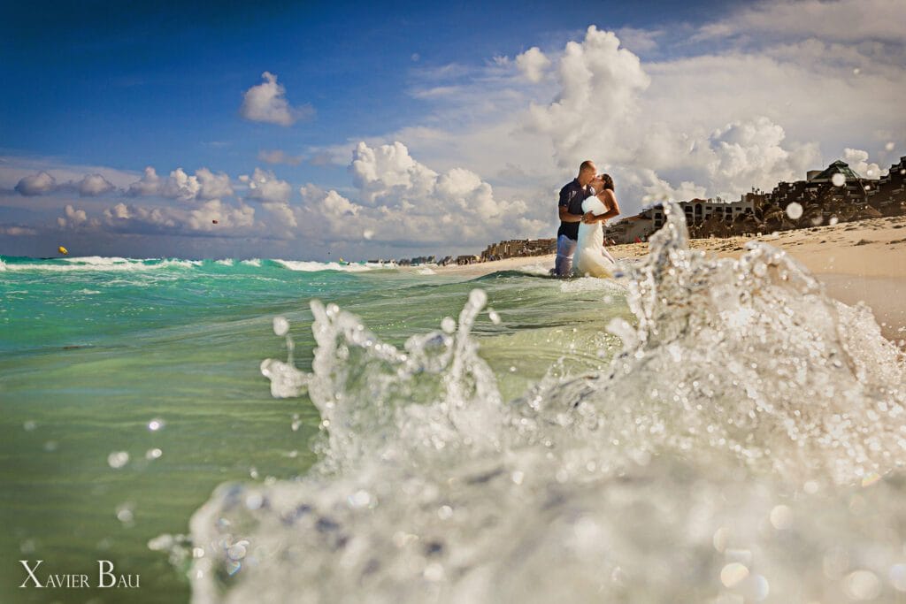 Bride and groom kissing in the turquoise ocean water on the beach during a dramatic 'Trash the Dress' photography session in Playa del Carmen, Mexico.