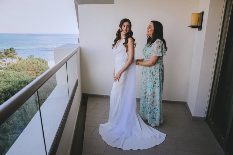Kishory in her white wedding dress with a guest on an ocean-view balcony.