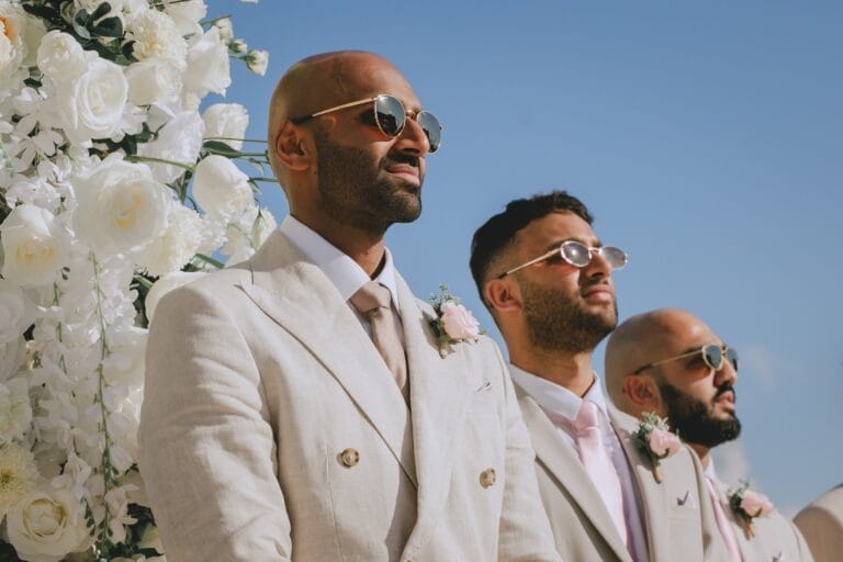 Kyle and his wedding party in light suits beside white ceremony flowers.