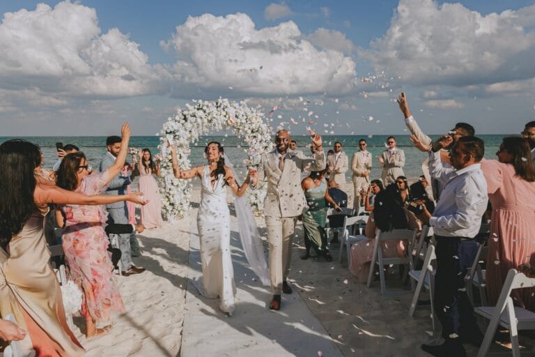 Kyle and Kishory walking through flower petals after their beach ceremony.