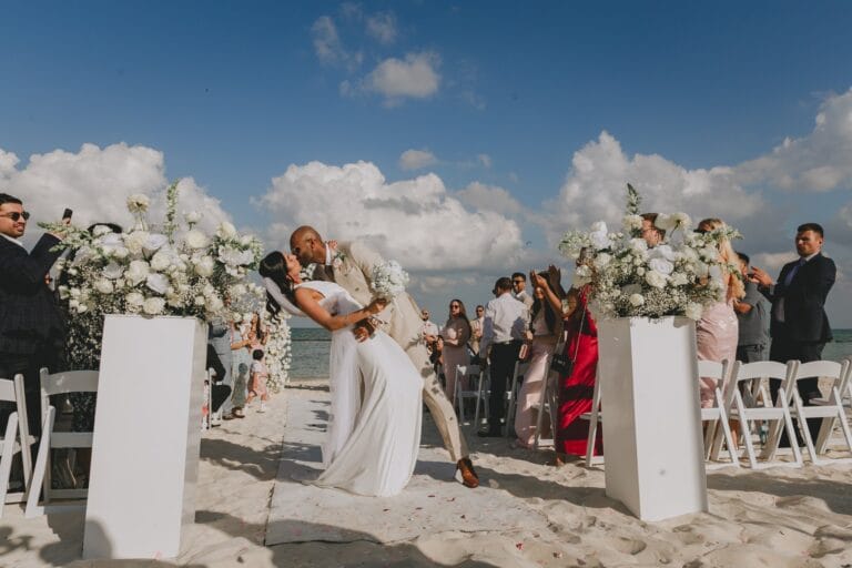 Kyle dipping Kishory for a kiss between the white floral arrangements.