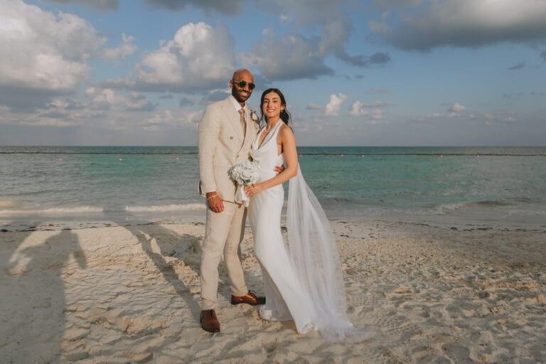 Kyle and Kishory standing together on the beach in their ceremony outfits.