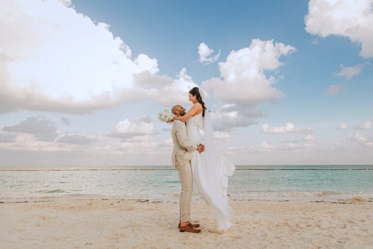 Kyle lifting Kishory beside the sea beneath a cloud-filled sky.