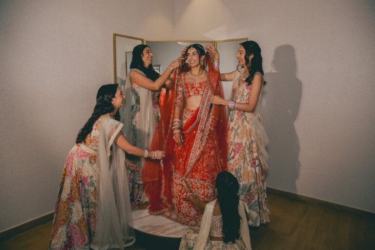 Kishory’s wedding party helping arrange her red lehenga and dupatta.