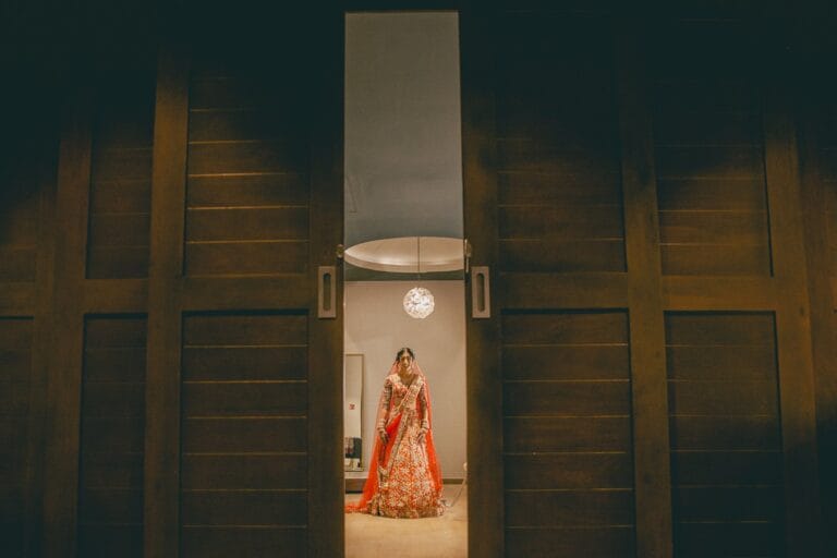 Kishory in a red lehenga framed by tall wooden doors at Dreams Natura.