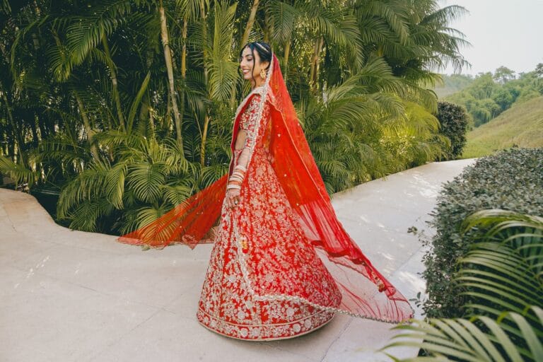 Kishory looking back on a garden path as her red dupatta trails behind her.