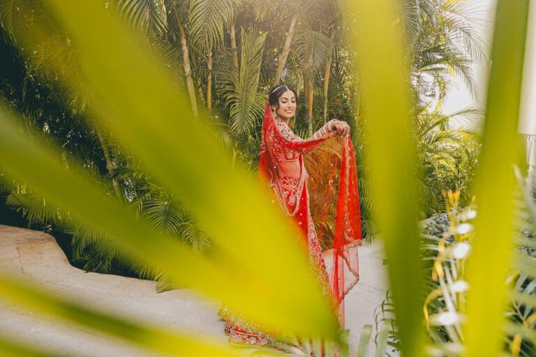 Kishory in her red lehenga photographed through palm leaves.