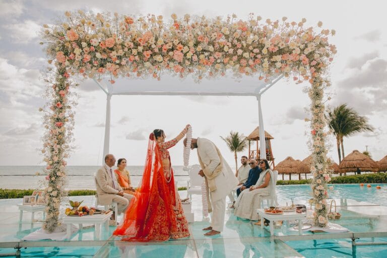 Kyle and Kishory standing beneath a pastel floral mandap over the pool.