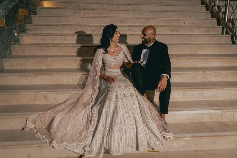 Kishory in an embellished evening outfit and Kyle in a dark suit on the staircase.