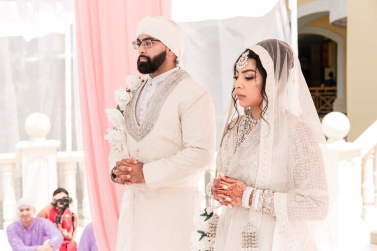 Nusaibah and Jai standing together beneath pale pink ceremony drapery at Barcelo Riviera Maya.