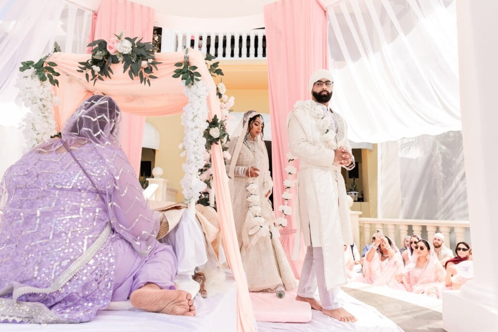 Nusaibah and Jai standing beneath pale pink drapery during their Sikh wedding ceremony.