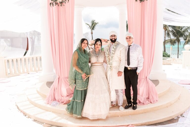 Nusaibah and Jai posing with two guests beneath pale pink drapery at Barcelo Riviera Maya.