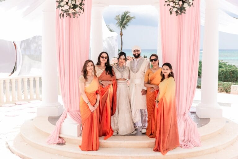 Nusaibah and Jai posing with guests in colorful dresses beneath the gazebo at Barcelo Riviera Maya.