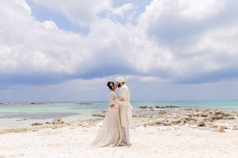 Wide beachfront portrait of Nusaibah and Jai beneath a cloud-filled sky at Barcelo Riviera Maya.