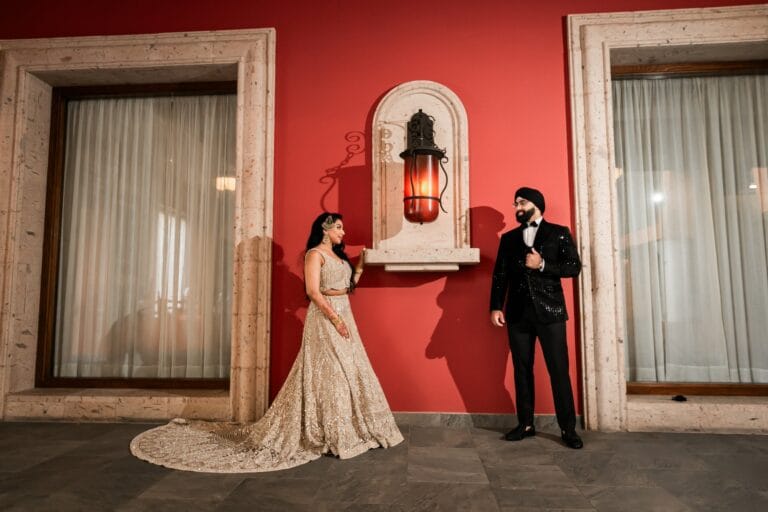 Nusaibah and Jai in evening wedding attire beside a red hotel wall at Barcelo Riviera Maya.