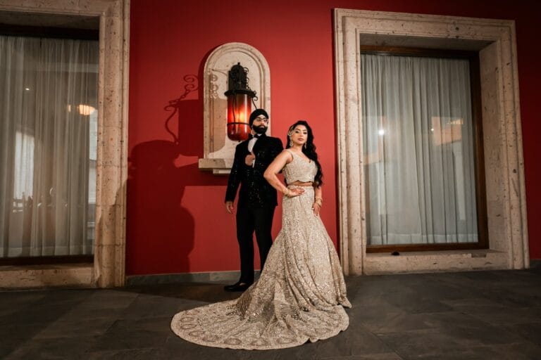 Full-length evening portrait of Nusaibah and Jai beside a red hotel wall at Barcelo Riviera Maya.