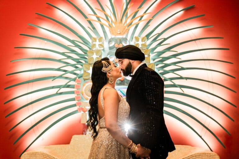 Nusaibah and Jai kissing before a decorative fan-shaped wall at Barcelo Riviera Maya.